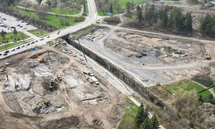 Vue aérienne, au printemps, du chantier de construction du stationnement à étages du nouveau campus de L’Hôpital d’Ottawa. Les équipes de construction creusent le sol à l’aide de pelleteuses et d’autres équipements lourds. 