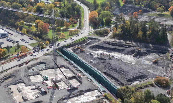 An aerial view in fall of the construction site where the parking garage for The Ottawa Hospital’s new campus is being built. A large tower crane is on site and parts of the concrete foundation have been poured at ground level. 