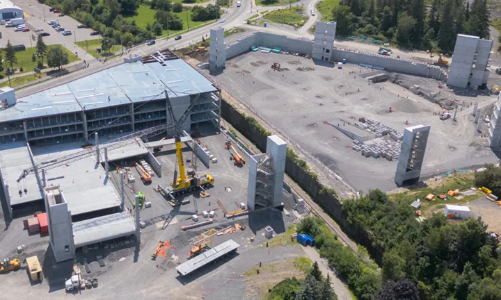 Vue aérienne, en été, du stationnement à étages partiellement construit sur le nouveau campus de L’Hôpital d’Ottawa. Une grande grue jaune se trouve sur le site et plusieurs niveaux ont été construits sur une moitié de la structure. Un toit inachevé recouvre la partie terminée. 