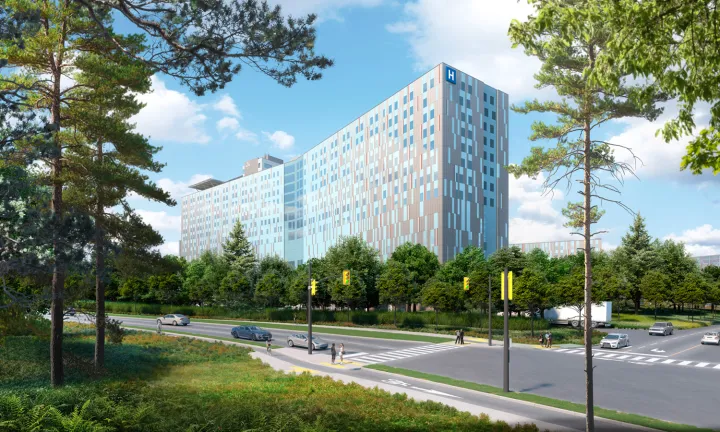 An artist rendering of The Ottawa Hospital’s new campus during the day, showing the left side of the exterior of the hospital. Trees in the foreground on the left and right sides frame the hospital in the centre. A road with vehicles on it runs left to right in front of the hospital, leading to an intersection with traffic lights at lower right.