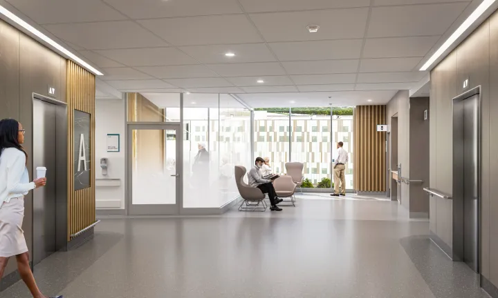 An artist rendering of a hallway inside a new hospital. The hall runs up the middle from the foreground to the background. Elevators are on either side of the hallways at left and right. In the background, there are chairs and large windows showing a clear view of the outdoors. On the left side of the background, a small room has glass walls which are gradually frosted on the lower half. People are standing and seated in various locations throughout the scene. 