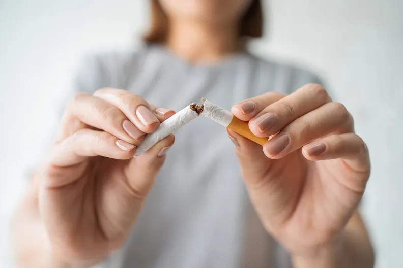 Une personne vêtue d’une chemise grise brise une cigarette en deux de ses deux mains, dans un geste symbolisant l’abandon du tabagisme. Les mains et la cigarette sont le point focal de la photo, dont l’arrière-plan est flou.