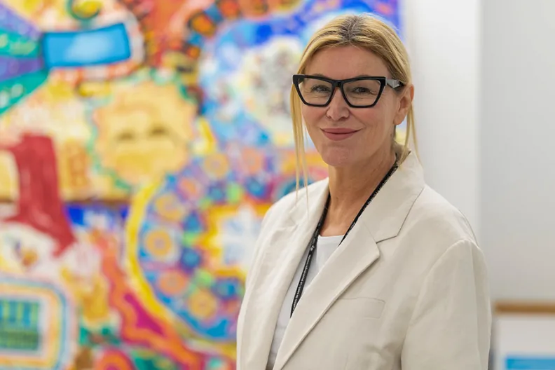 Dr. Mary Marquardt stands in front of some colourful, therapeutic artwork created by clients in the OnTrack program.