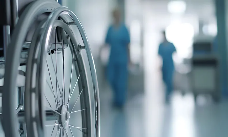 Close-up of a wheelchair in a hospital hallway with medical staff in the background.
