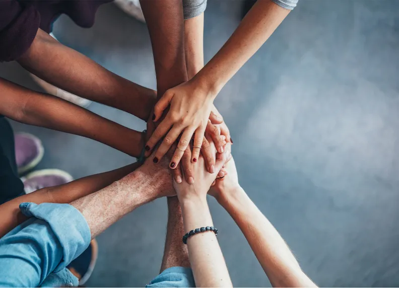 A group of people place their hands together in the center of a circle, symbolizing teamwork and unity.