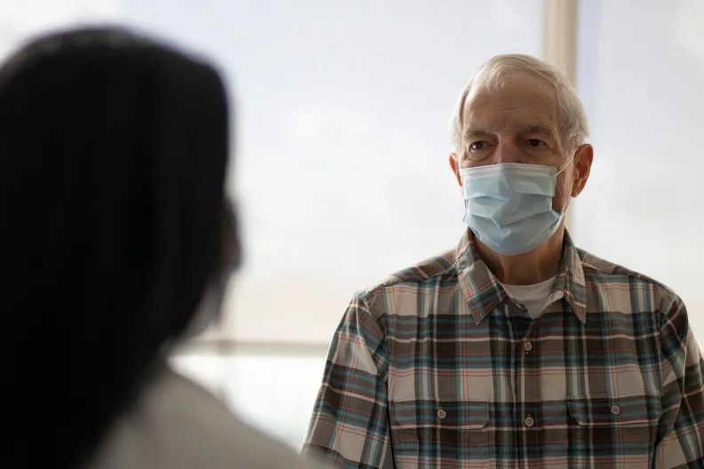 Un professionnel de la santé parle avec une personne âgée portant un masque. 