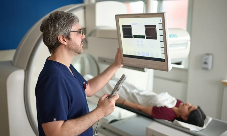 Un professionnel de santé utilise un panneau de commande tactile tandis qu’une patiente est allongée sur la table d’examen d’un appareil d’imagerie médicale en environnement clinique.