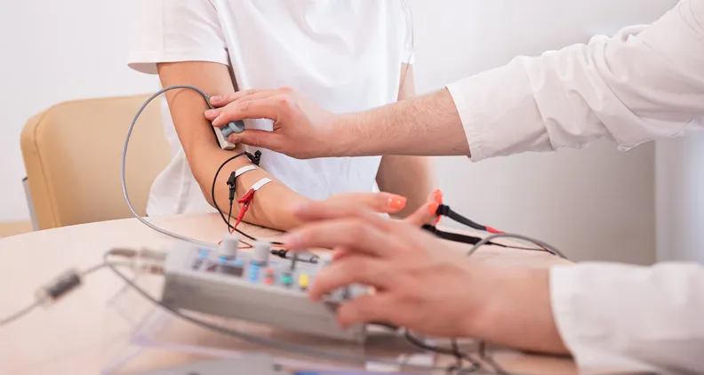 Un professionnel de la santé utilise des électrodes et un équipement de surveillance pour effectuer un test de la fonction nerveuse ou musculaire sur l’avant-bras d’une patiente.