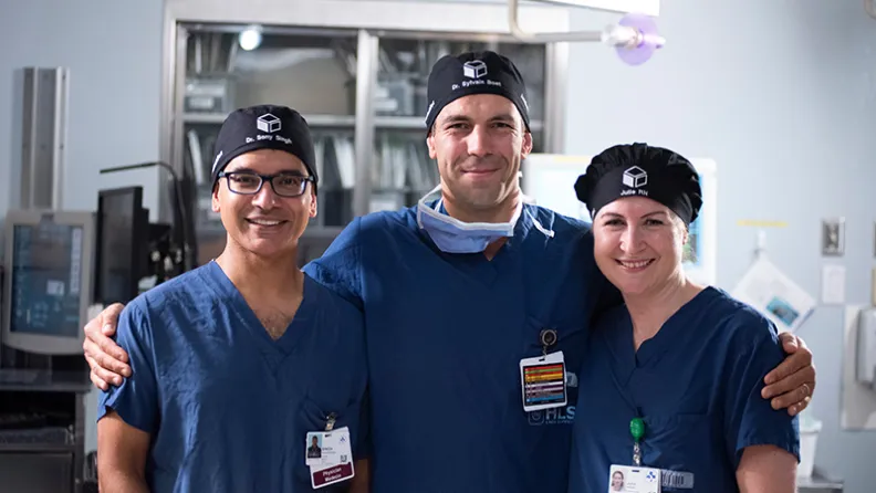 Trois membres du personnel de L’Hôpital d’Ottawa en tenue chirurgicale se tiennent ensemble dans un environnement hospitalier.