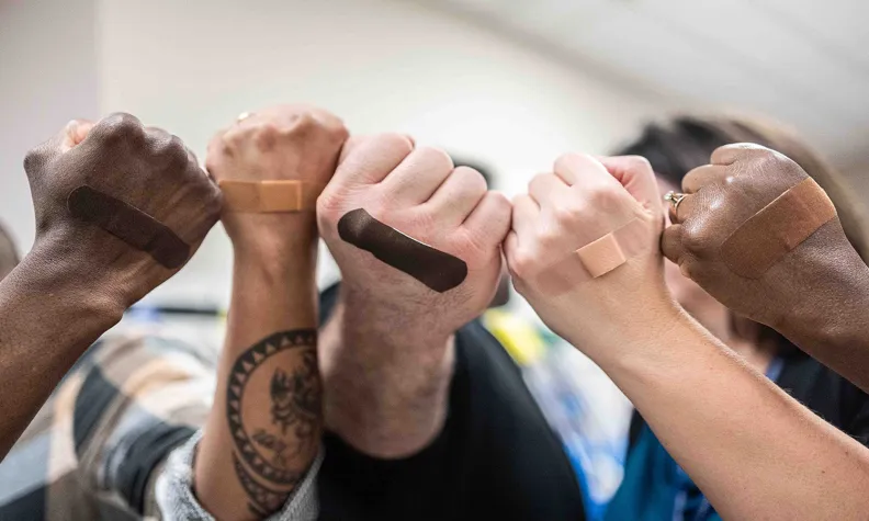 Hands showing different skin‑tone bandages on their arms, raised together in a row.
