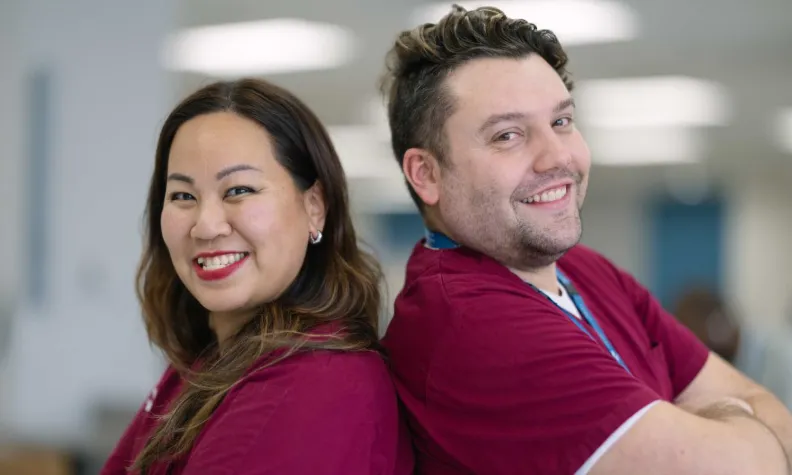 Two people wearing matching maroon scrubs stand back‑to‑back in a workplace setting.