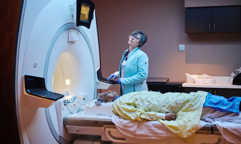 Patient lying on a table entering an MRI scanner while a technician operates the machine.