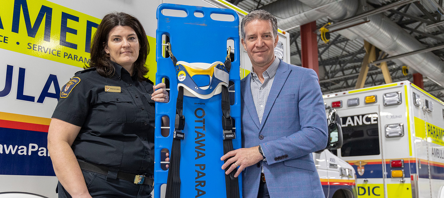 Paramedic Commander Shannon Leduc (left) and researcher Dr. Christian Vaillancourt (right) hold up a backboard and cervical collar.